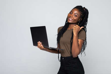 Photo of young african woman standing over gray wall with laptop computer.の写真素材