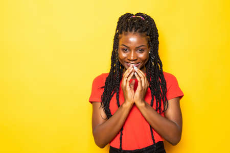 Beautiful african woman arms touch cheekbones look wondered empty space charming toothy smile isolated on yellow backgroundの写真素材