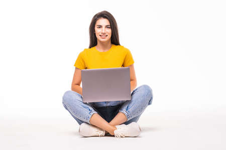 Happy young woman sitting on the floor and using laptop on white backgroundの写真素材
