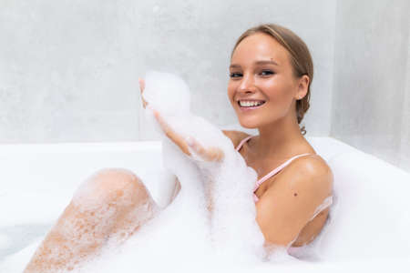 Attractive woman taking bath and playing with foam in bathroom