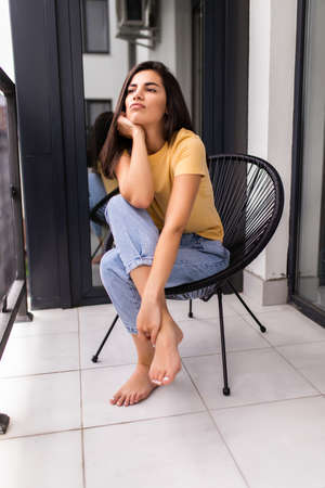 Relaxed woman is sitting on modern chair near the window in light cozy room at home enjoying peace...
