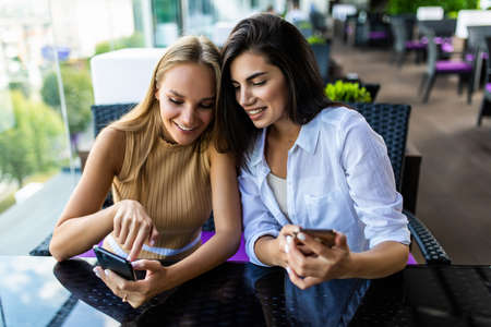 Two friends enjoying coffee together in a coffee shop and using phoneの写真素材
