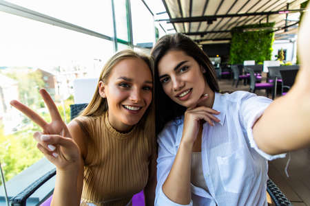 Two young women sitting in urban cafe and making selfie.の写真素材