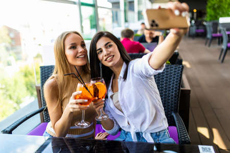 Two young woman take a selfie while sitting and chilling in the summer terrace of city cafeの写真素材