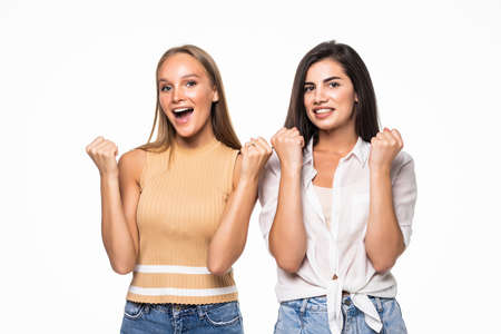 Two happy joyful young women posing standing clenching fists doing winner gesture keeping eyes closed isolated on white backgroundの写真素材