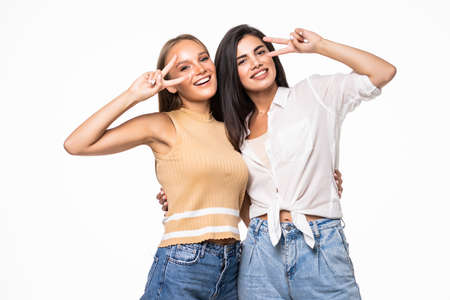 Picture of two playful girls standing together and showing peace gestures while looking at the camera over white backgroundの写真素材