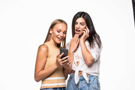 Two surprised cute young women using mobile phone together over white background