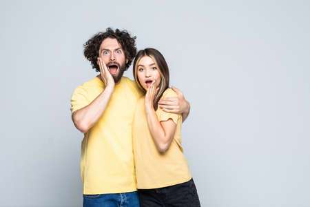 Happy excited couple standing with hands at their face and looking at camera over gray wallの写真素材
