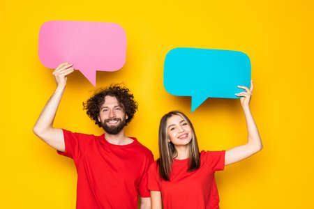 Young couple holding speech bubble over head on yellow backgroundの写真素材