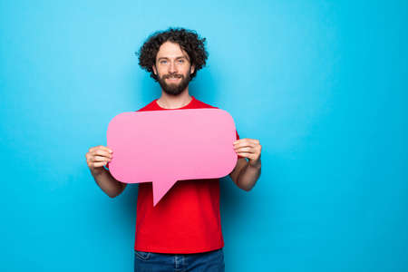 Photo of a handsome excited emotional adult man posing isolated over blue wall background holding speech bubble.の写真素材