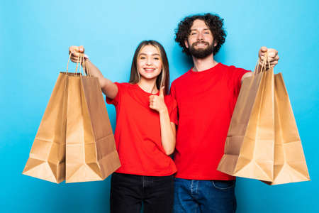 Attractive young couple with shopping bags on blue background, shopaholic person.の写真素材
