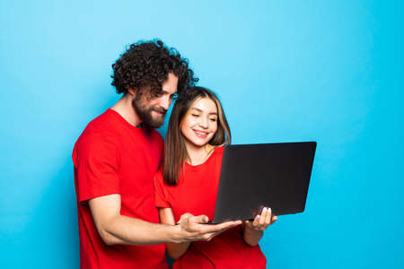 Portrait of a two happy young men and woman holding laptop computer over blue background.