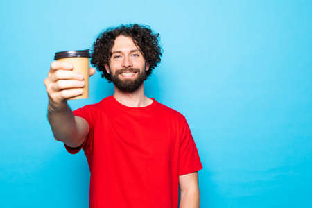 Portrait of a smiling young man holding cup of coffee isolated on a blue background.