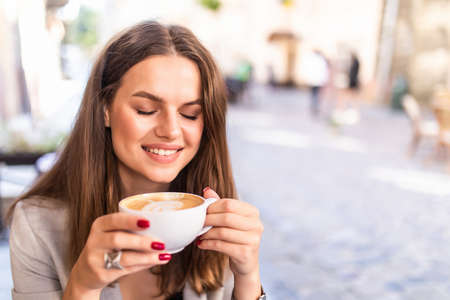 Portrait of young beautiful woman sitting in a cafe outdoor drinking coffeeの写真素材