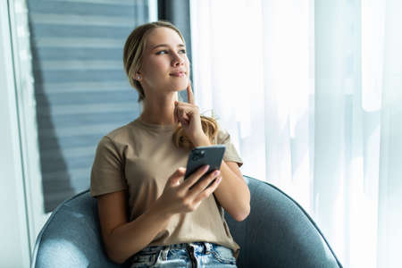 Lovely message from him. Beautiful young smiling woman looking at her smart phone while sitting in a...