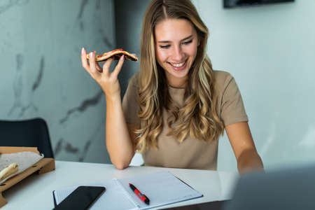 Overworked woman working on laptop and eating pizza, deadline