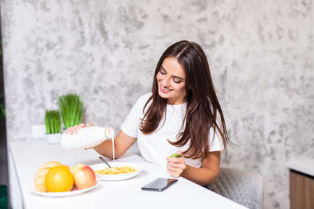 Smiling happy woman having a relaxing healthy breakfast at home sitting at kitchen table, she is...