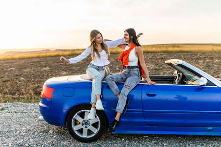 Young pretty two women sitting on convertible car and talking spend free time together.の写真素材