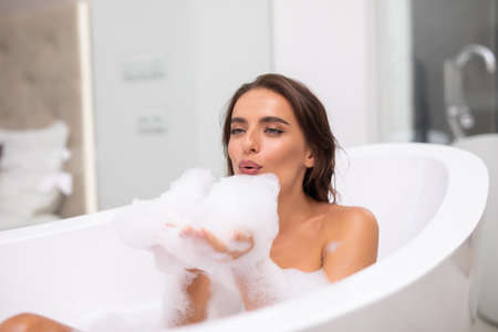 Portrait of happy young woman playing with foam in bathtub
