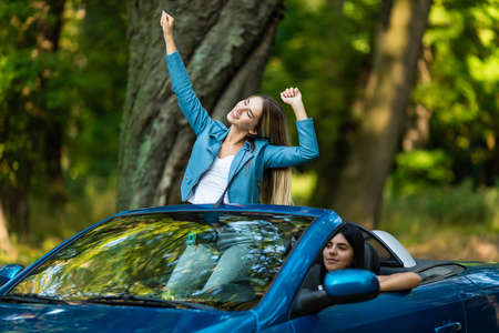 Free woman in cabriolet cheering joyful with arms raised. Woman going on road trip travel on summer dayの写真素材