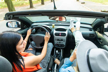 Rear view of two young women driving convertible car on summer road. Summer vocation.