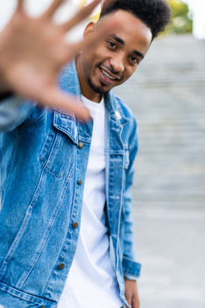 African man in a denim jacket on the streets waving his hand to a friendの写真素材