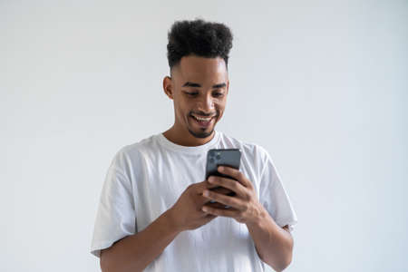 Happy African American man using phone, looking at screen, chatting with friends in social networks...