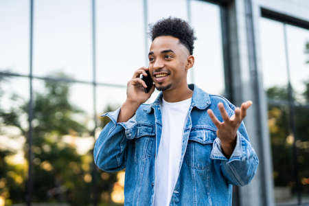 Young handsome Afro American man standing in front of huge modern business building smiling and...