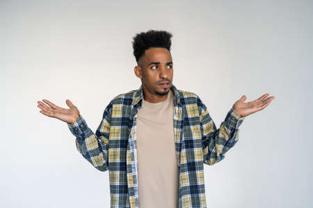 Portrait of young african american man gesturing do not know sign with confused expression. Isolated...