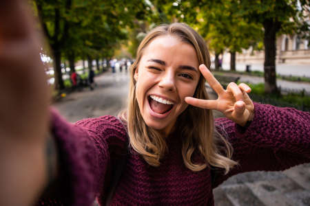 young attractive cheerful girl takes a selfie and makes peace sign with her fingersの写真素材