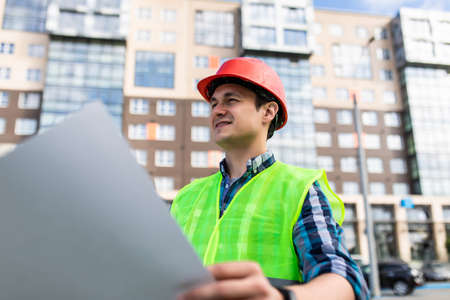 Confident architect holding rolled up blueprints at construction site