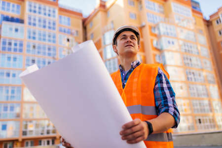 young professional engineer worker in protective helmet and blueprints paper on hand at the house...