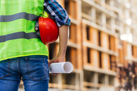 Close up of man engineer with blueprint and backhoe on the construction site