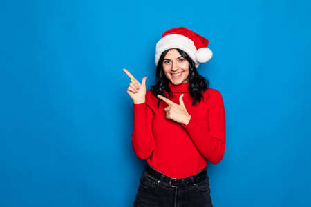 Woman with christmas hat isolated on blue background pointing to the side to present a product