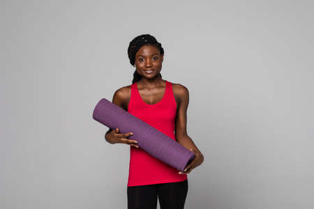 Young African American sport woman isolated on white background with a mat and smiling