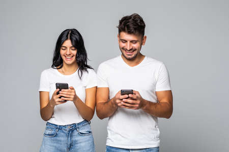 Internet addicted. Two young lovers are busy at their mobile phones in social nets, wearing casual...