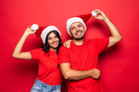 Cheerful couple in Santa Claus hats together isolated over red backgroundの写真素材
