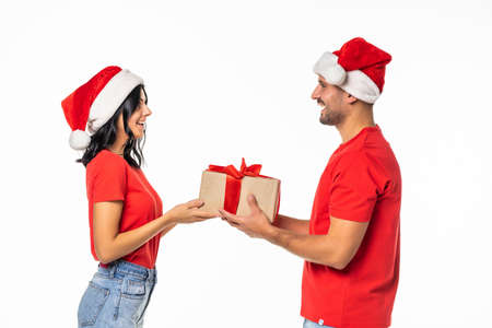 Excited happy couple with gift smiling looking to each other, wear red new year hat cap, isolated...