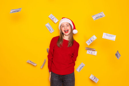 Laughing young woman Santa woman hold house, fan of cash money in dollar banknotes in Christmas hat posing isolated on red background. New Year 2020 celebration holiday concept. Mock up copy space.の写真素材