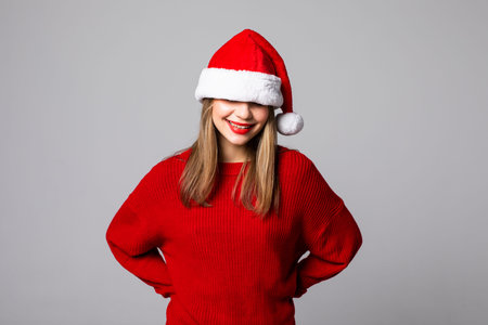 surprised woman with a christmas hat covering her eyes against a gray backgroundの写真素材