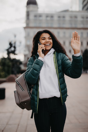 Portrait beautiful afro woman talk phone and wave hand outdoors.の写真素材