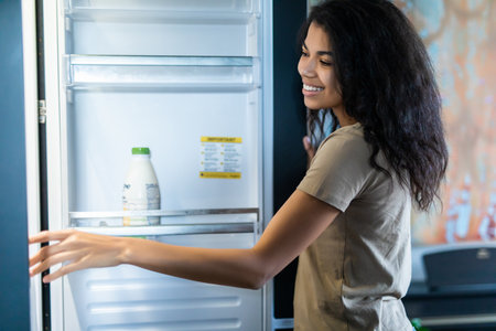 Young afro woman open fridge in the kitchenの写真素材