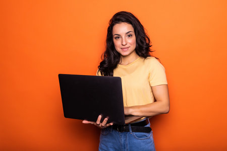 Surprised young woman working on laptop pc isolated on bright yellow background. People sincere...
