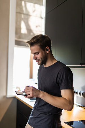 Side view of man using smartphone at table in kitchenの写真素材