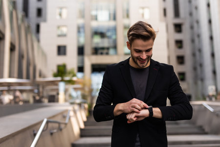 Confident male entrepreneur checking time on watch during break while hurrying for meeting, serious businessman in formal suit standing on urban settings with coffee takeaway looking at wristwatchの写真素材