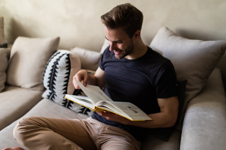 Smiling relaxed man reading a book lying on sofaの写真素材