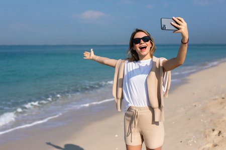 Young woman in summer clothes make video call on the phone at beachの写真素材
