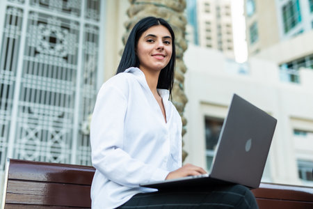 Side view portrait of a happy businesswoman checking laptop sitting on a benchの写真素材