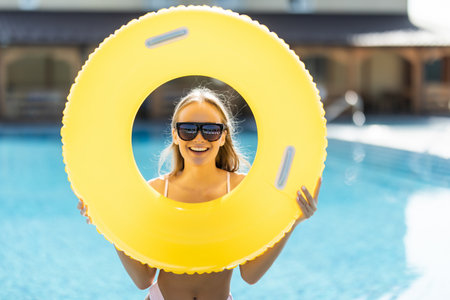 Beautiful woman in bikini holding a inflatable ring at poolside and smiling. Female wearing bikini...