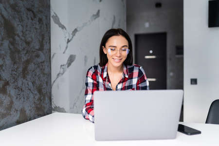 Shot of pretty young woman working with laptop and documents in the kitchen at home.の写真素材
